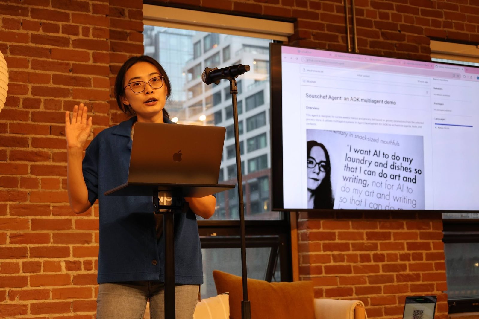 A presenter at a lectern demoing an AI agent, with the project shown on a screen